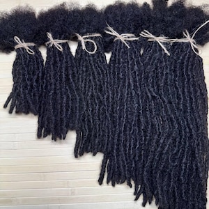 May include: A set of six bundles of black hair extensions featuring a textured, coiled appearance. Each bundle is secured at the top with a thin, light-colored string tied in a bow, with the hair lengths arranged in a staggered, ascending order.