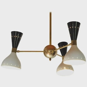 Peut inclure: Un lustre de style milieu du siècle avec une finition en laiton et quatre luminaires. Les luminaires sont noirs et blancs, avec de petites perforations. Le lustre est suspendu à une sphère centrale.