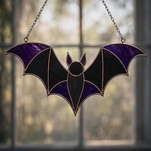 Peut inclure: Un attrape-soleil en vitrail en forme de chauve-souris avec des panneaux de verre noir et violet assemblés par des lignes de soudure en métal cuivré. La chauve-souris est suspendue par une fine chaîne métallique fixée au sommet des ailes.