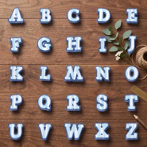 Könnte beinhalten: Ein vollständiger Satz von sechsundzwanzig Buchstaben des Alphabets, jeder mit einem hellblauen und weißen Zickzackmuster und einem einfarbig blauen Rand. Die Buchstaben sind in fünf Reihen angeordnet und zeigen das Alphabet von A bis Z in Blockschrift.