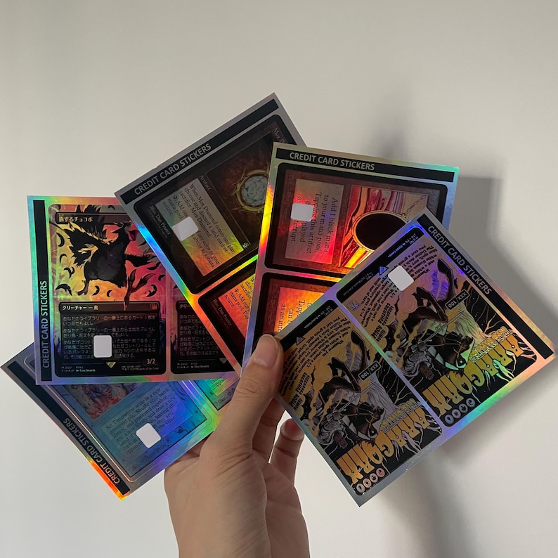 K&ouml;nnte beinhalten: Eine Sammlung rechteckiger Kreditkartenaufkleber mit holografischen Oberfl&auml;chen und verschiedenen Fantasy-Illustrationen. Jeder Aufkleber zeigt gedruckten Text, einschlie&szlig;lich der Worte CREDIT CARD STICKERS, sowie detaillierte Grafiken mit dunklen R&auml;ndern und lebendigen, reflektierenden Farbakzenten.