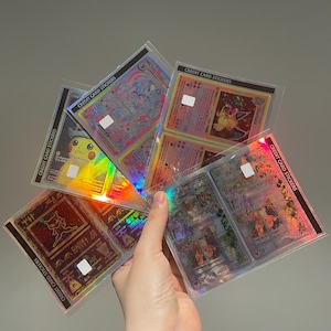Puede incluir: Una colecci&oacute;n de cartas coleccionables hologr&aacute;ficas, con varios personajes y dise&ntilde;os. Las cartas est&aacute;n en fundas protectoras, con el texto "CREDIT CARD STICKERS" visible. Las cartas tienen un acabado brillante e iridiscente.
