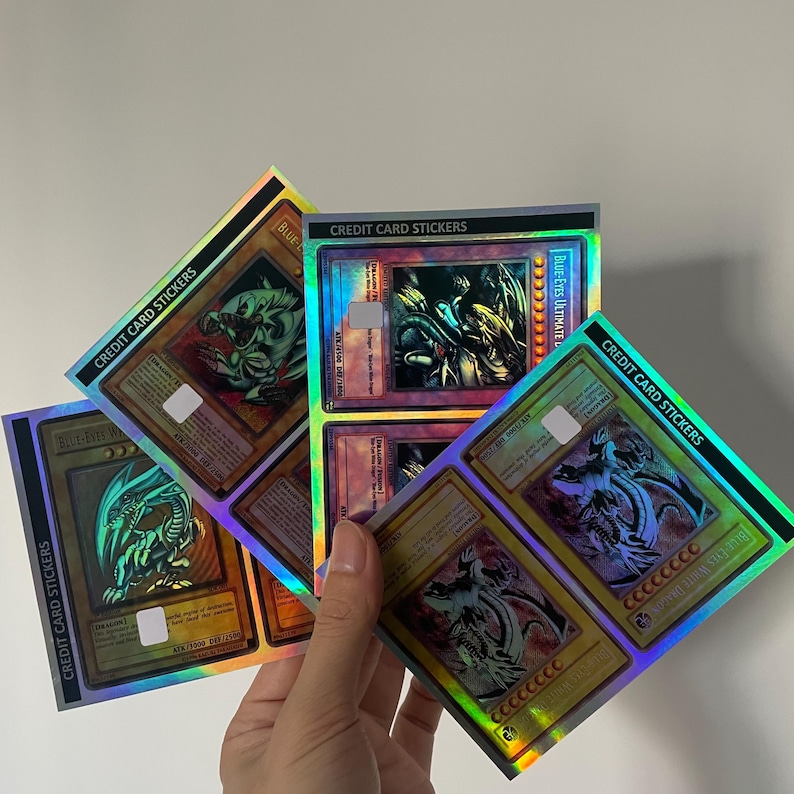 Pode incluir: Tr&ecirc;s adesivos retangulares para cart&atilde;o de cr&eacute;dito com acabamentos hologr&aacute;ficos e ilustra&ccedil;&otilde;es de cartas colecion&aacute;veis Yu-Gi-Oh!. Os designs exibem drag&otilde;es Blue-Eyes com bordas douradas e o texto CREDIT CARD STICKERS nas faixas pretas.