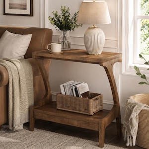 May include: A brown wooden console table with a Z-shaped frame, featuring a flat top surface and a lower shelf. The table holds a white ribbed table lamp, a white ceramic mug, and a rectangular woven wicker basket containing several magazines.