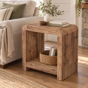 May include: A square wooden side table with a natural grain finish, featuring a flat top surface and a lower shelf. The table has rounded corners and a sturdy frame. A woven basket and two books are placed on the lower shelf for storage.
