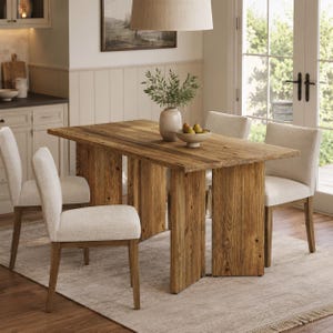 May include: A rectangular wooden dining table with a natural grain finish and two wide slab legs, accompanied by four upholstered chairs featuring cream-colored fabric and wooden legs. A ceramic vase with greenery and a bowl of pears sit on top.