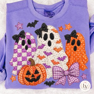 Könnte beinhalten: Ein lavendelfarbenes Sweatshirt mit Rundhalsausschnitt und drei gesteppten Geister-Applikationen mit schwarzen Schleifen sowie einem gesteppten orangefarbenen Kürbis. Die Geister sind mit lila Karos, schwarzen Punkten mit Fledermäusen.