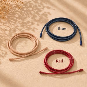 Op de afbeelding: Drie opgerolde koorden in beige, blauw en rood. Elk koord is voorzien van bijpassende eindkappen. Het blauwe koord is gelabeld met de tekst Blue en het rode koord met de tekst Red. Deze flexibele koorden zijn gerangschikt in cirkelvormige lussen.