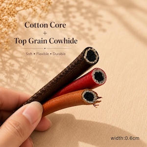 Op de afbeelding: Drie lengtes koord met een zwarte katoenen kern en een buitenkant van topnerf rundleer in donkerbruin, rood en tan. De tekst luidt Cotton Core + Top Grain Cowhide, Soft &bull; Flexible &bull; Durable, en width: 0.6cm.