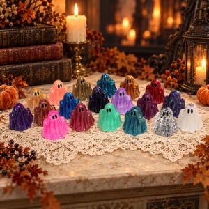 May include: A collection of small, ghost-shaped figurines in various colors including pink, blue, purple, green, white, and metallic tones. Each ghost features two black eyes and a smooth, glossy finish, arranged on a lace-trimmed surface.