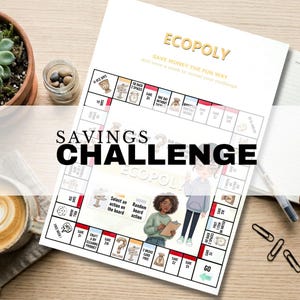Peut inclure: Un jeu de société de défi d'épargne "Ecopoly" blanc et doré avec le texte "Savings Challenge" en grandes lettres noires. Le plateau de jeu présente des illustrations et des invites pour économiser de l'argent. Une tasse de café et une plante succulente sont en arrière-plan.