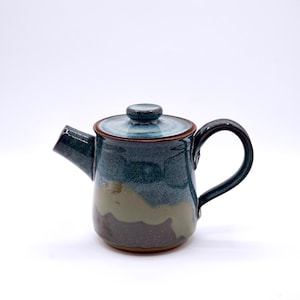 May include: A handcrafted ceramic teapot with a dark teal glaze, accented with brown and olive green hues. The teapot features a curved handle, a spout, and a lid with a small knob. This unique piece is perfect for brewing tea.