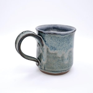 May include: A handmade ceramic mug with a blue and gray glaze. The mug has a rounded handle and a slightly textured surface. The base is a darker brown color. This stoneware mug is perfect for coffee or tea.