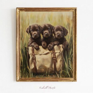 Puede incluir: Un óleo enmarcado que representa a tres cachorros de Labrador chocolate sentados dentro de un bolso de lona beige con correas de cuero marrón, sobre un fondo de hierba verde alta. El texto Foxhall Prints es visible en la parte inferior.