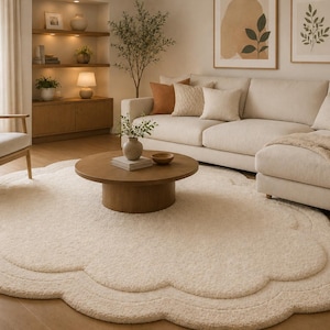 May include: A large, cream-coloured area rug with a scalloped, cloud-like edge and a textured, plush surface. The rug features a layered, concentric design that follows the curved perimeter, creating a soft, rounded shape on the floor.