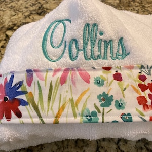 May include: White hooded towel with a floral print border and the name "Collins" embroidered in teal on the front.