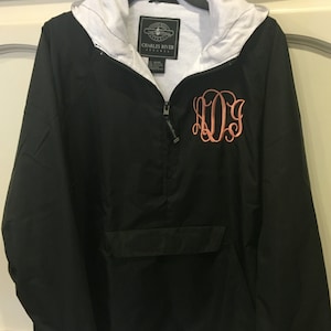 May include: Black hooded jacket with a white lining and a zipper closure. The jacket has a large pocket on the front and a monogrammed "KDS" in pink on the chest. The label on the jacket reads "Charles River Apparel".