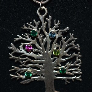 May include: A silver tree of life pendant necklace with five colorful gemstones. The gemstones are green, pink, blue, and a darker green.