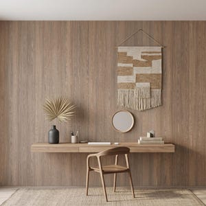 May include: A floating wooden desk with a matching wooden chair, a dark gray vase with a dried palm leaf, a small circular mirror, and a rectangular woven wall hanging with cream and tan geometric patterns mounted on a wood paneled wall.