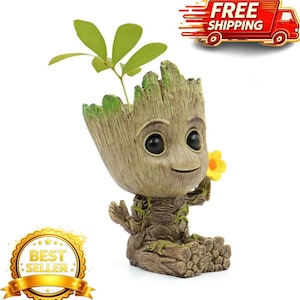 May include: A brown, tree-like planter shaped as a small humanoid figure with a textured bark surface, large black eyes, and a smiling expression. The figure holds a small yellow flower in one hand and has green leaves sprouting from its head.