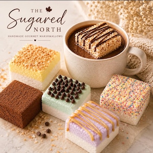 May include: A collection of square gourmet marshmallows from The Sugared North, including a yellow coconut-topped one, a cocoa-dusted one, a mint one with chocolate chips, a rainbow sprinkle one, a purple one with caramel drizzle, and one in hot cocoa.