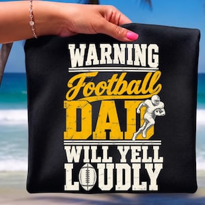 May include: A black t-shirt featuring the white and yellow text WARNING Football DAD WILL YELL LOUDLY. The design includes a graphic of a football player in a white uniform running with a football and a white illustration of a football below the text.