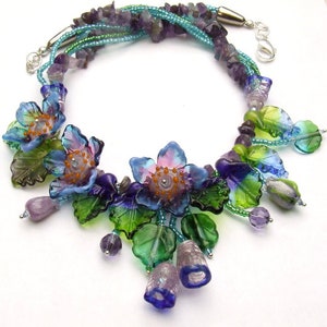 Pu&ograve; includere: Una collana multifilo con perline di ametista e fiori di vetro. I fiori sono blu, verdi e viola con un centro rosa. La collana &egrave; impreziosita da perline argentate e una chiusura argentata.