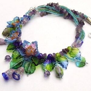 Pu&ograve; includere: Una collana multifilo con perline di ametista e fiori e foglie di vetro in tonalit&agrave; di blu, verde e viola.