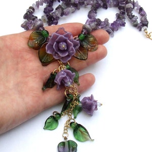 May include: A necklace featuring a strand of purple amethyst chip beads and a central pendant arrangement of three carved purple glass roses and several green glass leaves, all connected by gold-toned metal links and small jump rings.