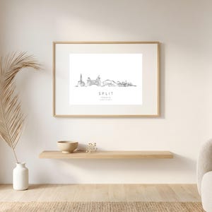 Könnte beinhalten: Ein rechteckiger gerahmter Kunstdruck mit einer schwarzen Strichzeichnung der Skyline von Split, Kroatien. Der Text unter der Illustration lautet SPLIT, CROATIA, gefolgt von geografischen Koordinaten. Der Rahmen besteht aus hellem Holz.