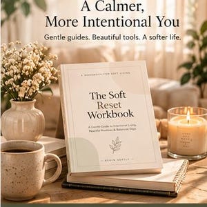 Könnte beinhalten: Ein beigefarbenes Arbeitsbuch mit dem Titel The Soft Reset Workbook und einer Blattillustration, das auf einem Tisch neben einer gesprenkelten Keramiktasse, einer Vase mit Trockenblumen und einer brennenden Kerze in einem Glas steht.