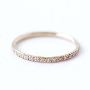 May include: A delicate gold band ring with a row of small diamonds set in a pave setting.