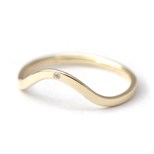 May include: A delicate gold band ring with a single small diamond set in the center. The band is curved in a wave shape.