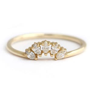 K&ouml;nnte beinhalten: Ein zarter Goldring mit f&uuml;nf klaren, marquisef&ouml;rmigen Edelsteinen. Der Ring hat ein d&uuml;nnes, poliertes Band, und die Edelsteine sind in einem gebogenen, kronenartigen Design gefasst. Der Ring ist vor einem wei&szlig;en Hintergrund.