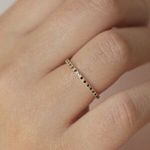May include: A delicate gold band ring with a row of small black diamonds.