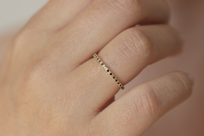 May include: A delicate gold band ring with a row of small black diamonds.
