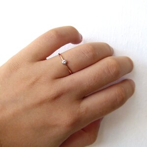 以下が含まれることがあります： 小さな透明な宝石が1つ付いたシンプルなゴールドバンドリングです