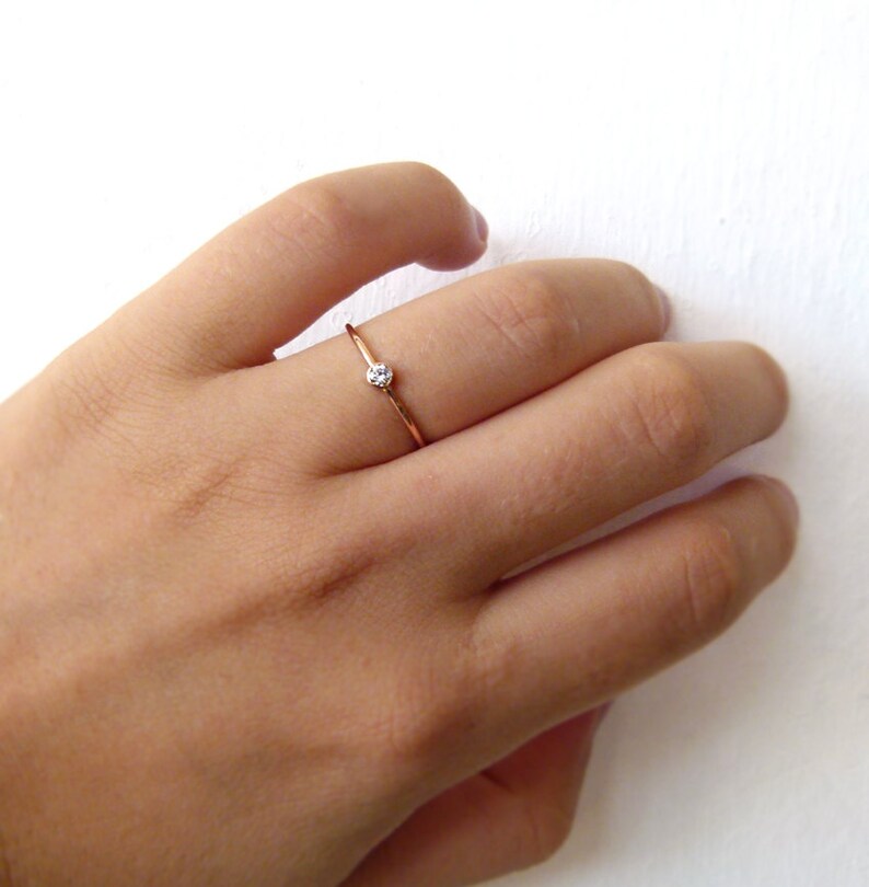 以下が含まれることがあります： 小さな透明な宝石が1つ付いたシンプルなゴールドバンドリングです