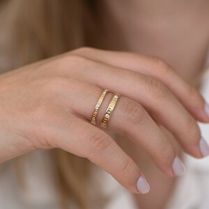 Puede incluir: Dos anillos de oro con peque&ntilde;os diamantes en un dedo. El anillo de abajo tiene una banda texturizada y el anillo de arriba tiene una banda lisa.