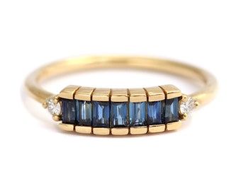 May include: A gold band ring with a row of blue sapphire baguette stones and two small diamond accents.