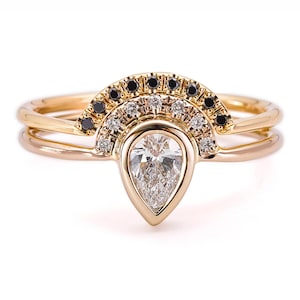 May include: A pear-shaped diamond engagement ring set with a delicate band. The ring features a halo of small diamonds and black diamonds.