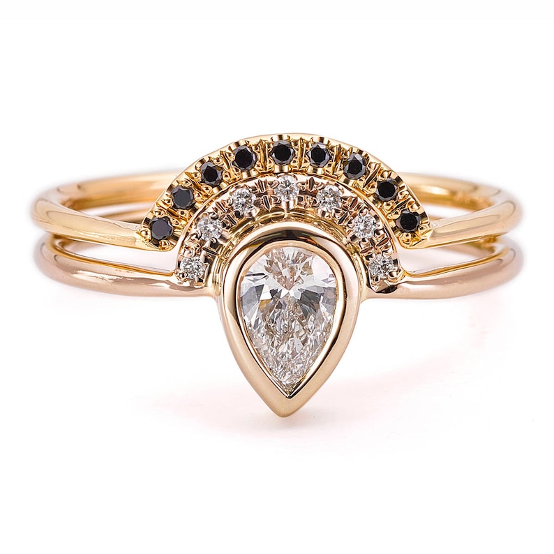 May include: A pear-shaped diamond engagement ring set with a delicate band. The ring features a halo of small diamonds and black diamonds.