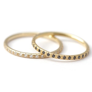 May include: Two gold wedding bands with a row of small diamonds. One band has white diamonds and the other has black diamonds.