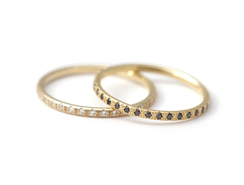May include: Two gold wedding bands with a row of small diamonds. One band has white diamonds and the other has black diamonds.
