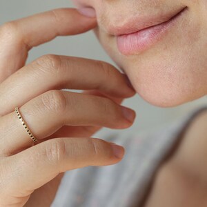 May include: A gold ring with a textured band. The ring is worn on the finger of a person's hand.