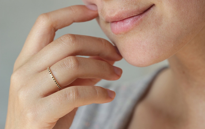 May include: A gold ring with a textured band. The ring is worn on the finger of a person's hand.