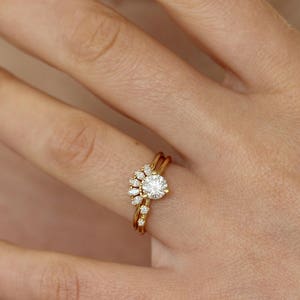 K&ouml;nnte beinhalten: Ein goldener Ringsatz mit einem runden, klaren Edelstein als Mittelpunkt, erg&auml;nzt durch kleinere, klare Edelsteine in f&auml;cherf&ouml;rmiger Anordnung. Das Set enth&auml;lt ein gebogenes Band mit zus&auml;tzlichen kleinen Edelsteinen.