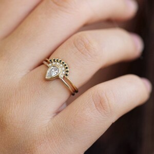 May include: A pear-shaped diamond engagement ring with a delicate band, paired with a matching band featuring a row of black diamonds.