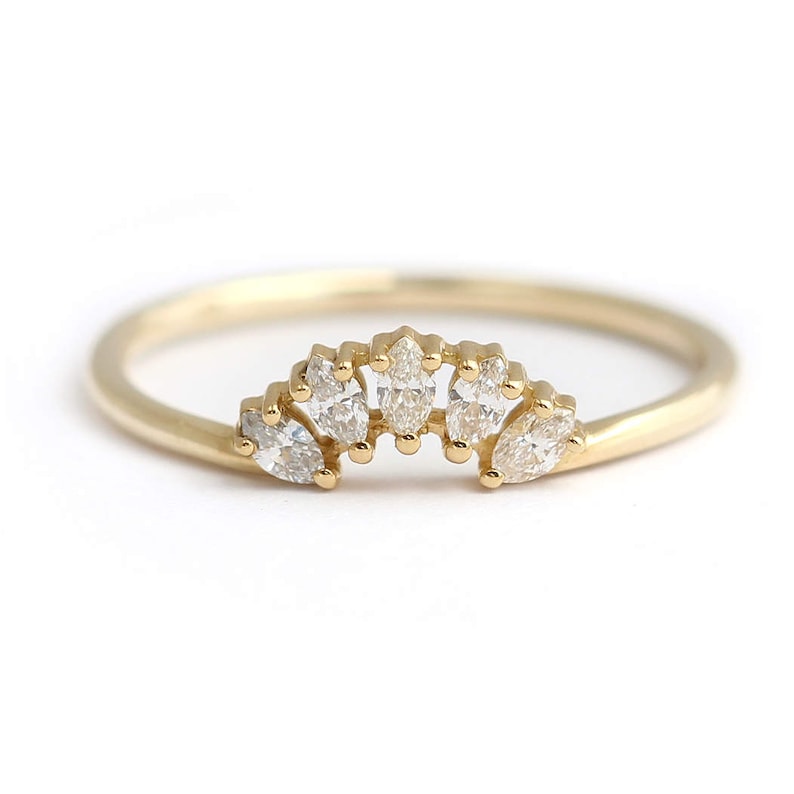K&ouml;nnte beinhalten: Ein zarter Goldring mit f&uuml;nf klaren, marquisef&ouml;rmigen Edelsteinen. Der Ring hat ein d&uuml;nnes, poliertes Band, und die Edelsteine sind in einem gebogenen, kronenartigen Design gefasst. Der Ring ist vor einem wei&szlig;en Hintergrund.
