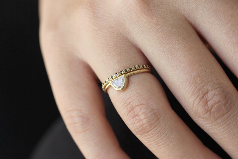 May include: A gold ring set with a half-moon shaped diamond and a thin band of black diamonds.